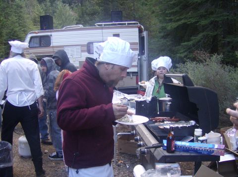 1986 Ford Bronco - A group of people in chef hats are gathered around a grill, preparing food at an outdoor event with a trailer in the background.