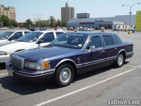 1994 Lincoln Town Car - A dark blue sedan is parked in a lot next to a white sedan under a clear sky.