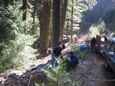 1989 Ford Bronco - People are cleaning up trash in a wooded area next to a blue SUV.
