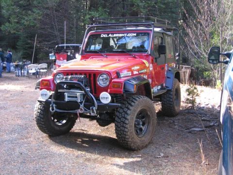1989 Ford Bronco - A modified red Jeep Wrangler is parked outdoors, with a rack on top and a winch on the front bumper.