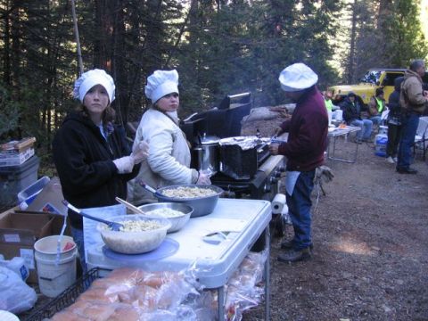 1989 Ford Bronco - Outdoor cooking event with multiple people preparing and serving food, a yellow vehicle is visible in the background.