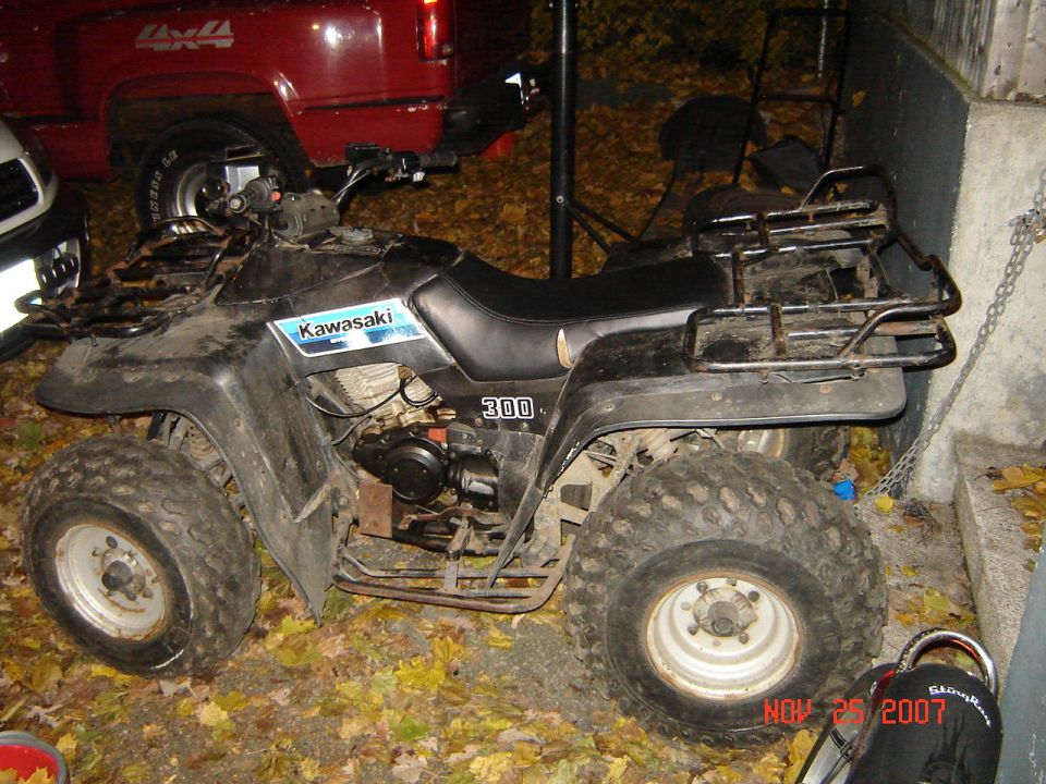 Black Kawasaki 300 four-wheeler ATV parked on leaves at night by a red truck