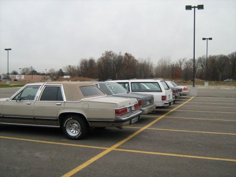 1988 Mercury Grand Marquis - A row of cars, including a 1988 Mercury Grand Marquis, are parked in an outdoor lot under an overcast sky.