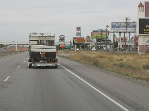 1989 Ford F-250 - A truck tows a large camper down the highway, passing by billboards and businesses.