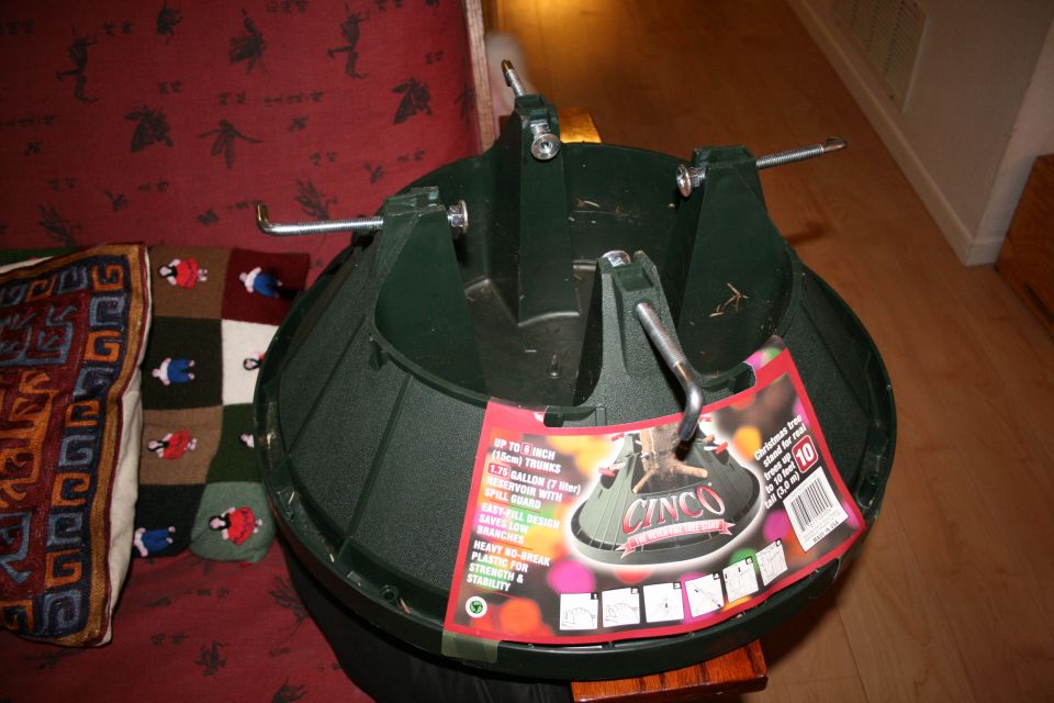 Green plastic Christmas tree stand with metal supports and a red label that says CINCO