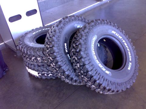 1995 Ford F-150 - Three BFGoodrich Mud-Terrain T/A tires with white raised lettering leaning against a white surface on a polished concrete floor. The aggres…