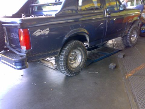 1995 Ford F-150 - Dark blue Ford 4x4 pickup positioned on a shop alignment rack, shown from the three-quarter rear with a '4X4' decal, 'FORD' tailgate letter…