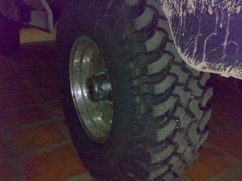 1995 Ford F-150 - Dim low-angle close-up of an oversized mud-terrain tire with deep aggressive lugs mounted on a polished aluminum wheel with a chrome lockin…