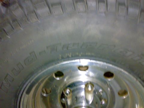 1995 Ford F-150 - Close-up of an aggressive Mud-Terrain tire sidewall and blocky tread mounted on a polished aluminum wheel with visible lug holes and hub. T…