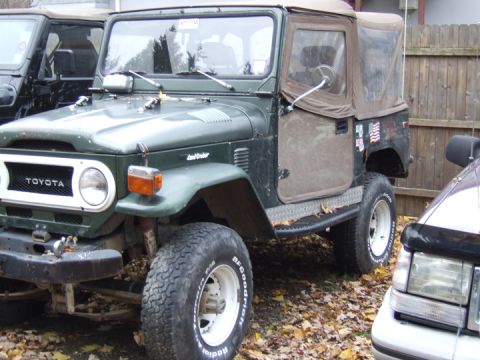 1976 Toyota Land Cruiser - A green Toyota Land Cruiser with a tan soft top is parked next to another vehicle.