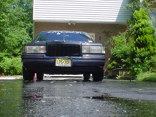 Dark blue Lincoln Town Car on a wet driveway in front of a brick house, front view