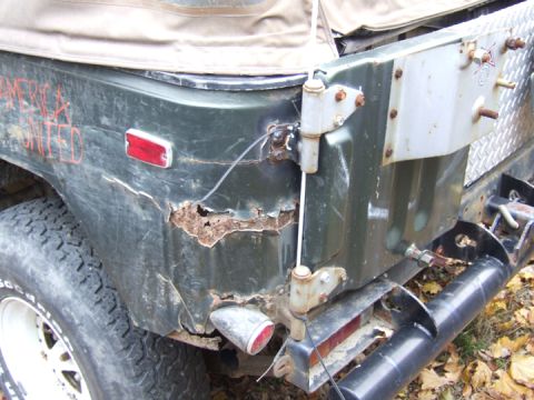 1976 Toyota Land Cruiser - The rear of a heavily rusted green off-road vehicle shows significant body damage and spray-painted text.