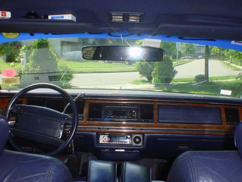 1994 Lincoln Town Car - The dashboard features wood grain trim and a large infotainment screen, with a view of a residential street through the windshield.