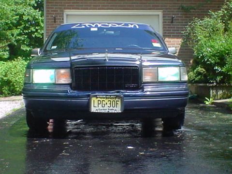 1994 Lincoln Town Car - This Lincoln Town Car is parked in front of a brick garage on a wet surface.