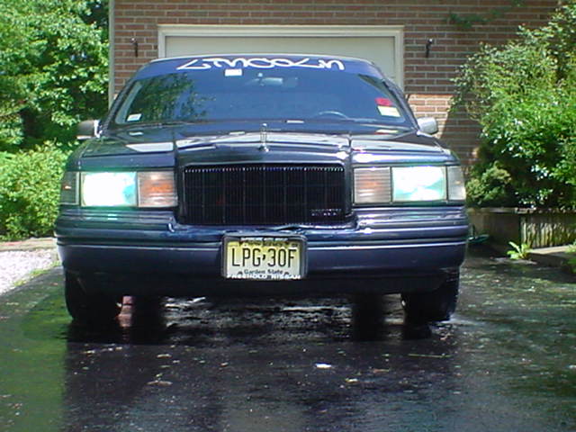 Front view of dark blue Lincoln Town Car with lights on and yellow New Jersey plate LPG-30F