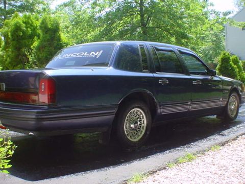 1994 Lincoln Town Car - A dark blue Lincoln Town Car is parked on the side of the road with trees in the background.