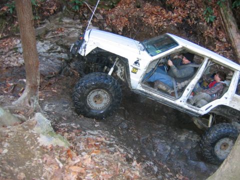 1992 Ford Mustang - Modified Jeep Cherokee tackling a challenging off-road obstacle on a wooded trail.