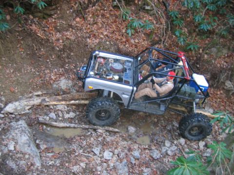 1992 Ford Mustang - This heavily modified off-road vehicle navigates a challenging trail with logs and rocks.