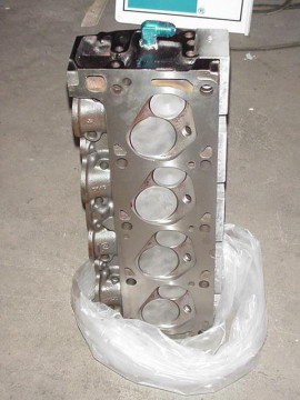 1972 Ford Ranchero - A close-up view of an engine cylinder head, resting in a plastic bag on a concrete floor.