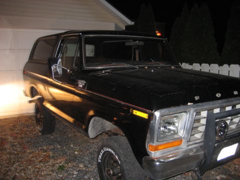 1991 Ford Bronco - A black Ford Bronco is parked in front of a garage, with its headlights on.