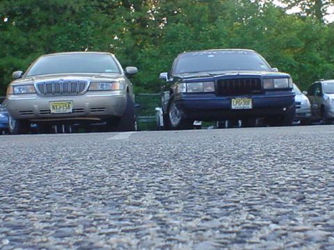 1994 Lincoln Town Car - Two full-size sedans are parked side-by-side on a paved surface with trees in the background.