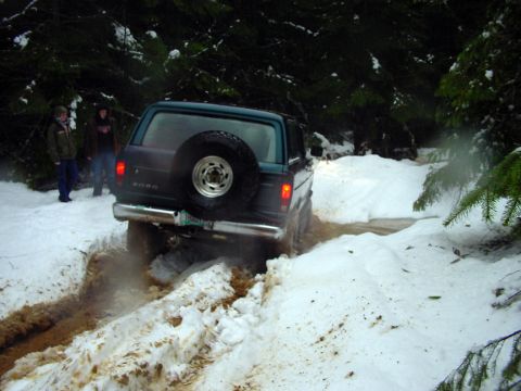 1979 Ford Bronco - A 1979 Ford Bronco navigates a snowy and muddy trail in a wooded area.