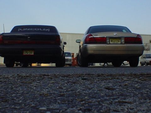 1994 Lincoln Town Car - Two sedans are parked side-by-side, viewed from the rear. The car on the left has 'LINCOLN' visible on its rear window.