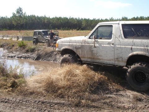 1989 Ford Bronco - A white Ford Bronco navigates a muddy obstacle course alongside a Jeep.