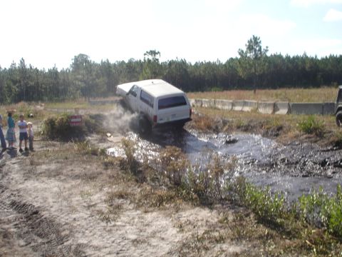 1989 Ford Bronco - White 1989 Ford Bronco navigates a muddy obstacle course, kicking up water and dirt.