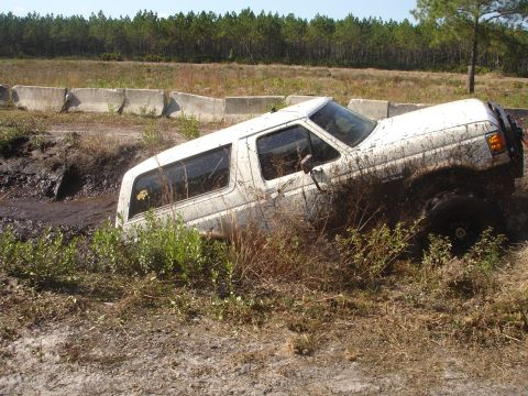 1989 Ford Bronco - This vehicle appears to be stuck in a muddy off-road course, with its tires submerged in the mire.
