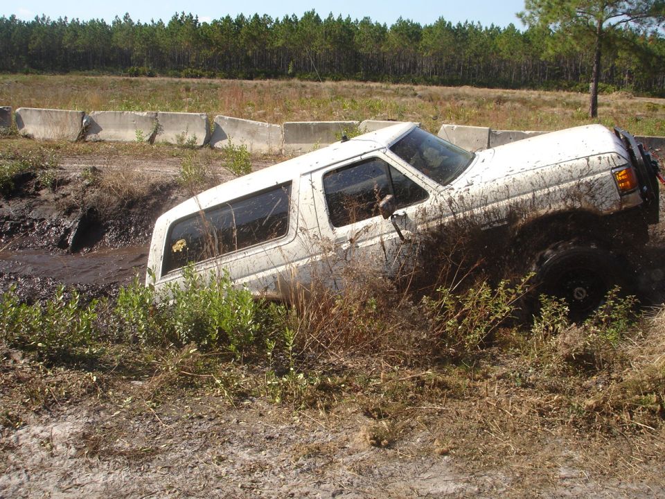 White SUV stuck in a muddy ditch, tires sunk deep