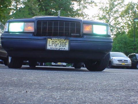 1994 Lincoln Town Car - A dark sedan is parked in a lot, with its front end facing the camera and headlights illuminated.