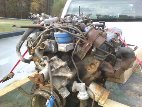 1979 Ford Ranchero - A heavily rusted engine with a blue distributor cap is loaded onto a flatbed truck.