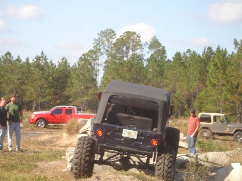 1989 Ford Bronco - A dark blue Jeep Wrangler navigates an obstacle course with other vehicles and people present.