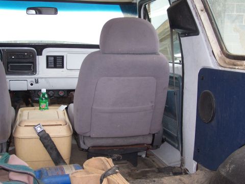 1979 Ford Bronco - The interior of a vehicle shows a driver's seat, dashboard, and a cooler with a drink on top.