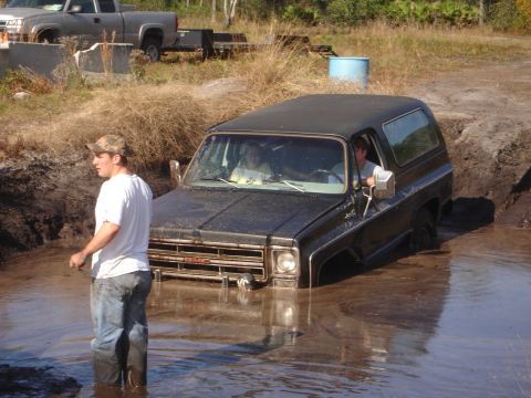 1989 Ford Bronco - A black GMC Jimmy is stuck in the mud with a person in the driver's seat and another standing nearby.