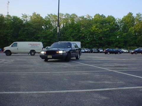 1994 Lincoln Town Car - A dark sedan is parked in a lot with a white van and other vehicles visible.