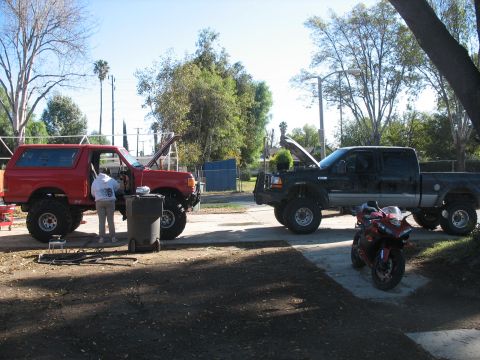 2001 Ford F-250 - Two trucks and a motorcycle are parked outside on a sunny day, with one person working on the red truck.
