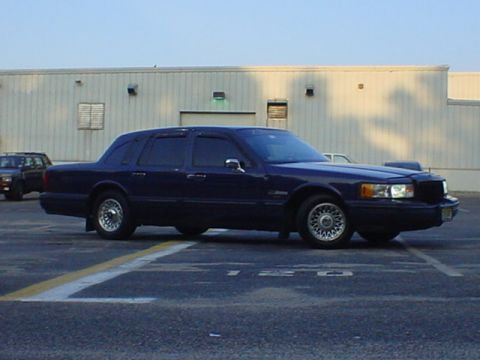 1994 Lincoln Town Car - A dark blue sedan is parked in a lot with a building behind it and another vehicle in the distance.