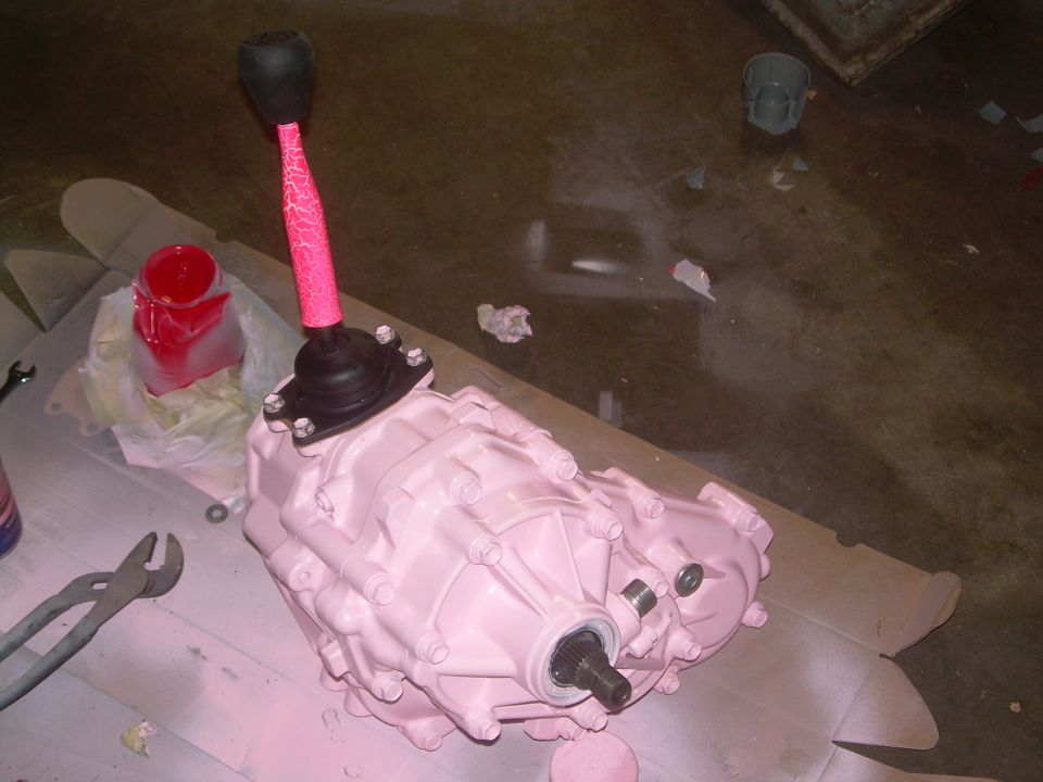 Transfer case painted pink with a pink textured shifter boot and black knob. Pliers and a jar of red liquid are nearby