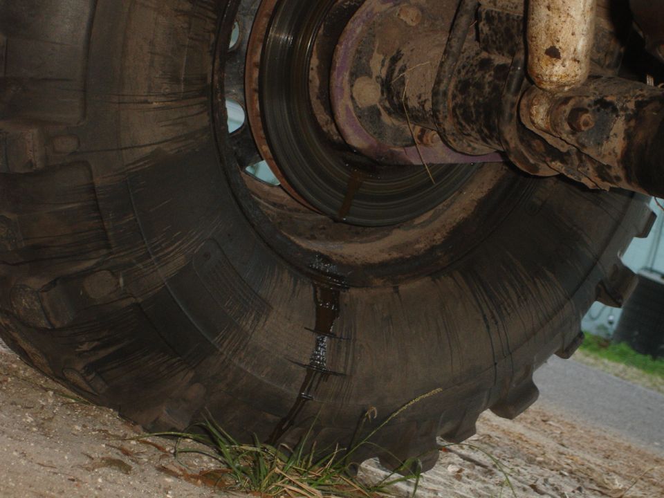 Close-up of a large, muddy tire and part of the vehicle's suspension system. Some fluid is leaking