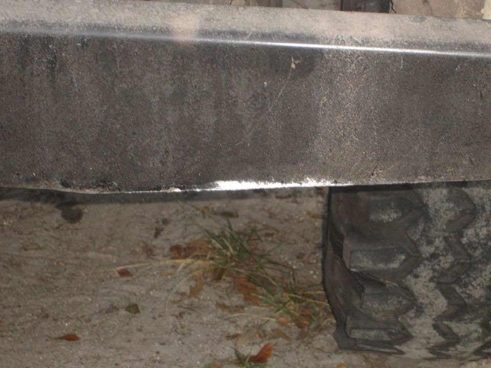 Close-up of a dark gray textured bumper with a chrome strip below it, and a tire tread visible on the right