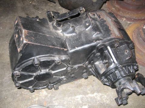 1989 Ford Bronco - A black cast-iron transfer case sits on a concrete garage floor, removed from the vehicle, with its bolted rear output housing, front outpu…
