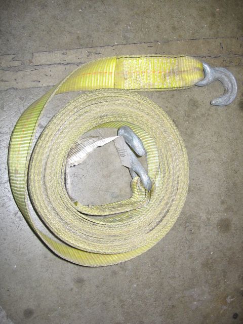 1989 Ford Bronco - A yellow tow strap with two metal hooks is coiled on a concrete surface.