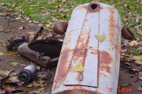 1946 Ford F1 - Disassembled vehicle parts, including a hood and radiator, are scattered on the ground amidst autumn leaves.