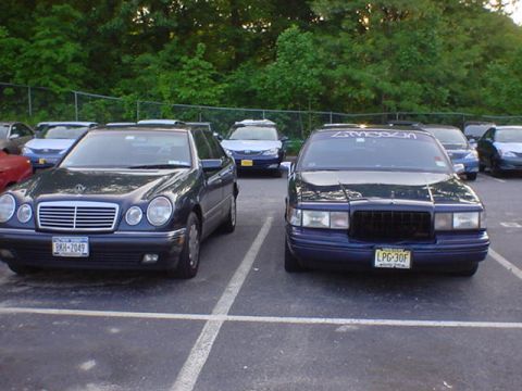 1994 Lincoln Town Car - Two sedans are parked side-by-side in a parking lot with trees in the background.