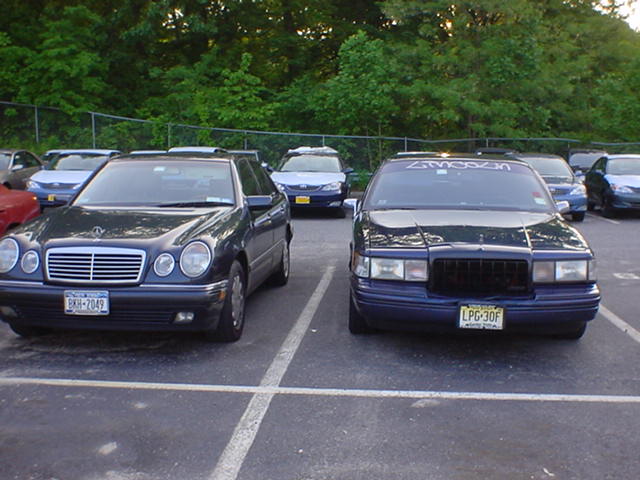 Black Mercedes E-Class parked beside dark blue Lincoln Town Car, both facing camera in a lot