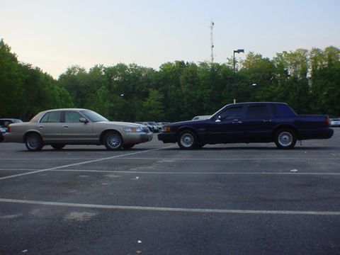 1994 Lincoln Town Car - Two sedans, one tan and one dark blue, are parked in a lot under a cloudy sky.