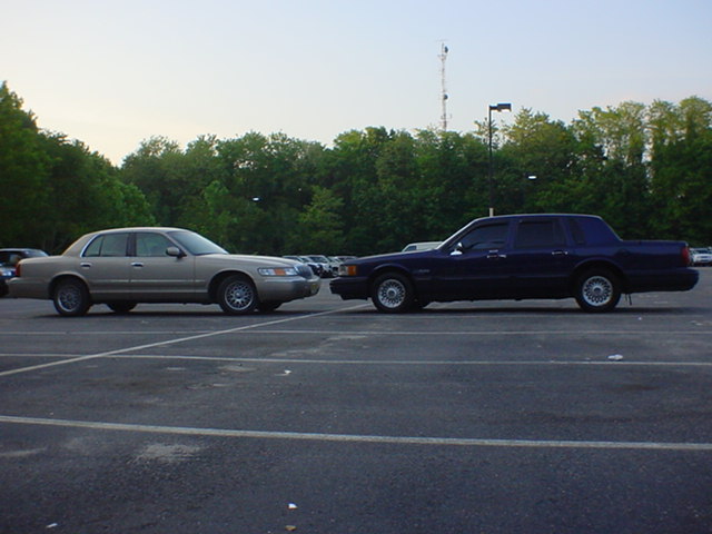 Gold Mercury Grand Marquis and dark blue Lincoln Town Car parked nose to nose in an empty lot