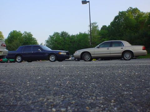1994 Lincoln Town Car - Two sedans are parked next to each other on a paved surface with trees in the background.